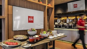 Ein reichhaltiges Buffet mit verschiedenen Speisen und einem großen Bildschirm, der das ibis-Logo zeigt.