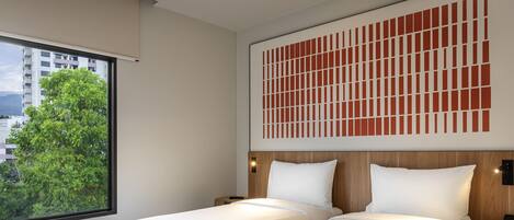 A hotel room with two beds, a large window with a view of buildings and trees, and a decorative wall panel.