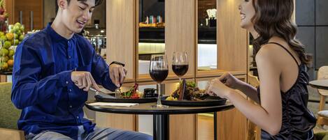 A man and a woman dining at a table with a meal, wine glasses, and a small plant on the table.