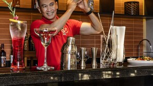Ein Barkeeper bereitet ein Getränk an der Bar zu, umgeben von verschiedenen Flaschen und Gläsern.
