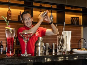 Un barman prépare un cocktail dans un bar où l’on peut voir différentes bouteilles et différents verres.