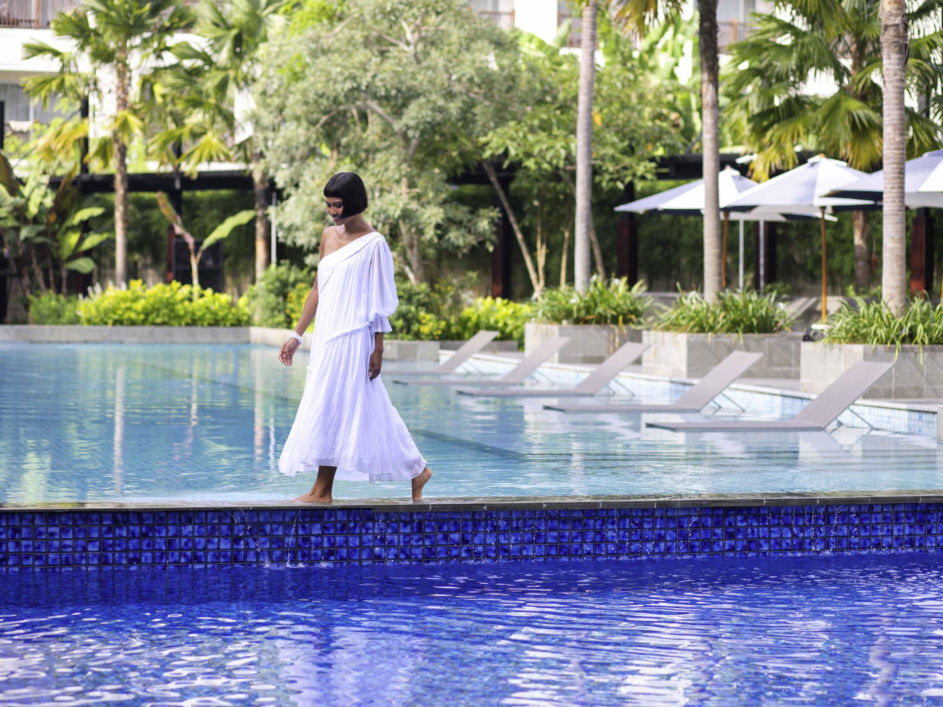 A person walking along the edge of a pool with a blue tiled border.