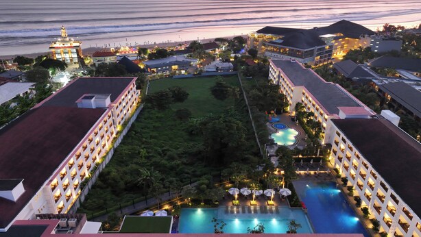 A resort with multiple buildings, a swimming pool, and a view of the ocean at sunset. - Grand Mercure Bali Seminyak (Seminyak)