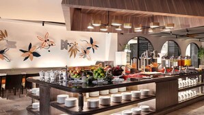 A buffet area with a variety of food items, including fruits and beverages, and a counter with stacked plates. - Grand Mercure Bali Seminyak (Seminyak)