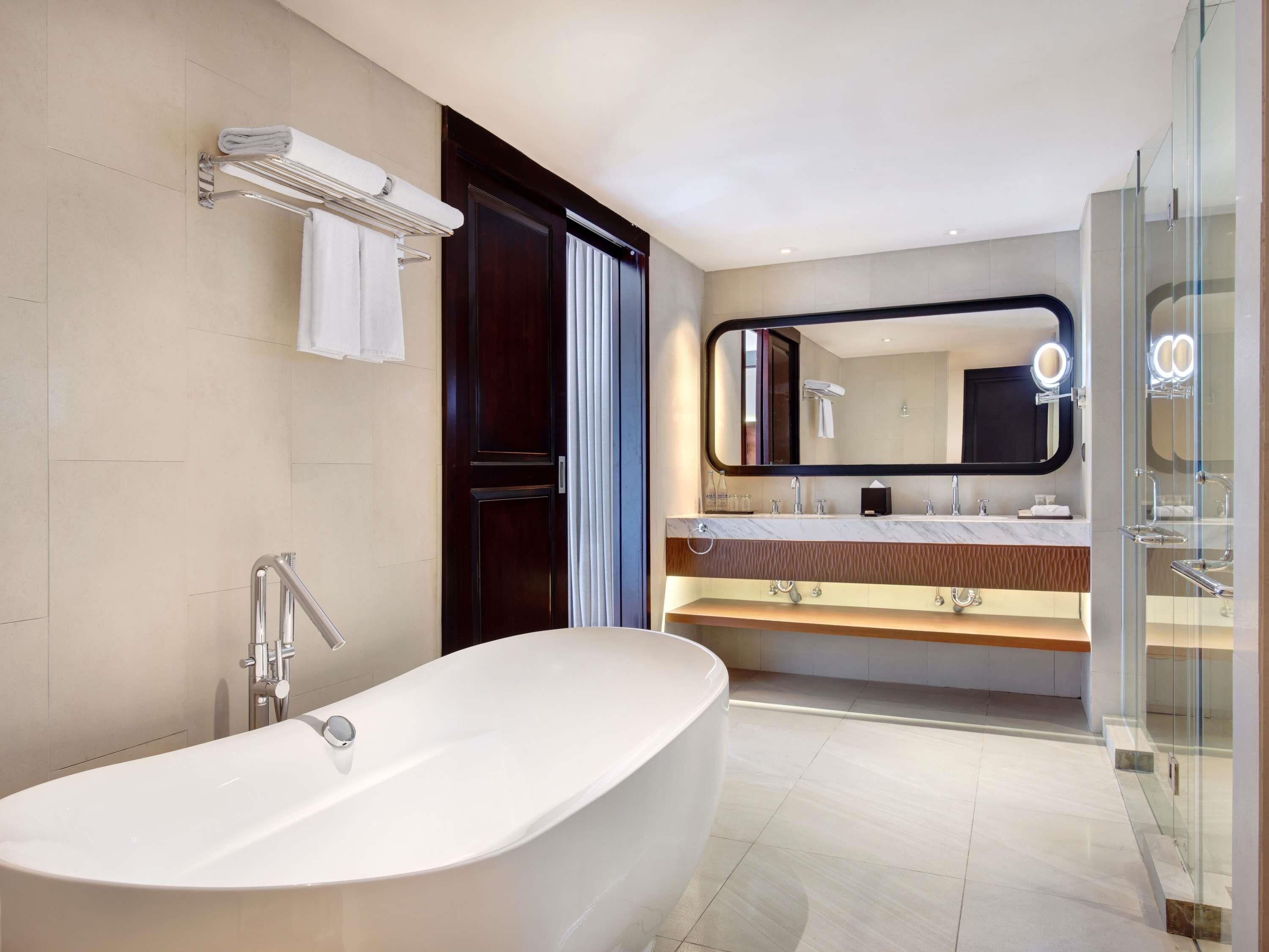Un baño moderno con una bañera independiente, un espejo grande con iluminación, un mueble de tocador con encimera de mármol y una cabina de ducha de vidrio.