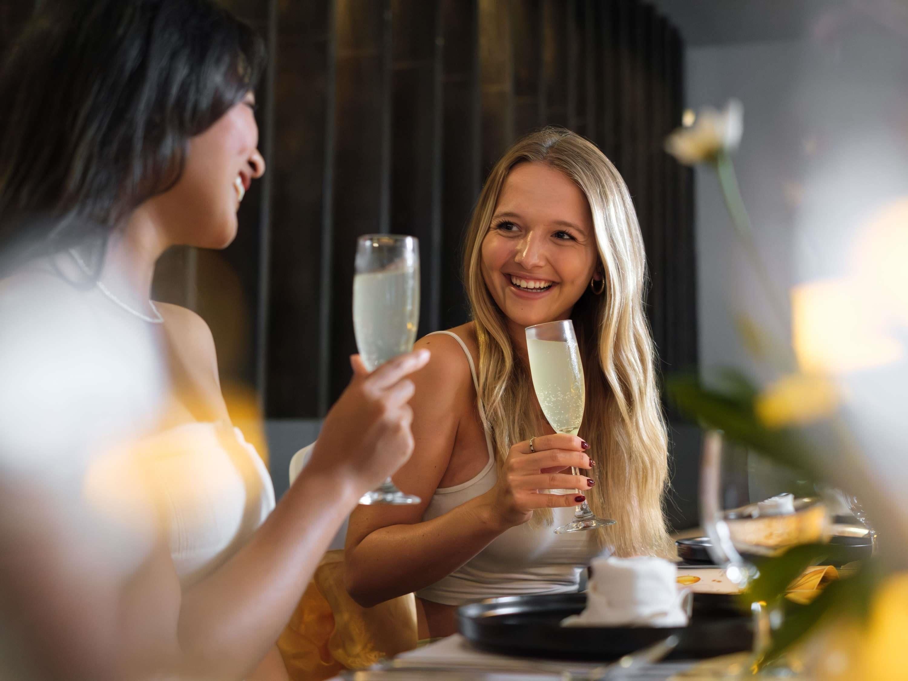 Kaksi henkilöä istuu pöydän ääressä, ja heillä on edessään lasi samppanjaa, mikä viittaa sosiaaliseen tilaisuuteen tai juhlaan.