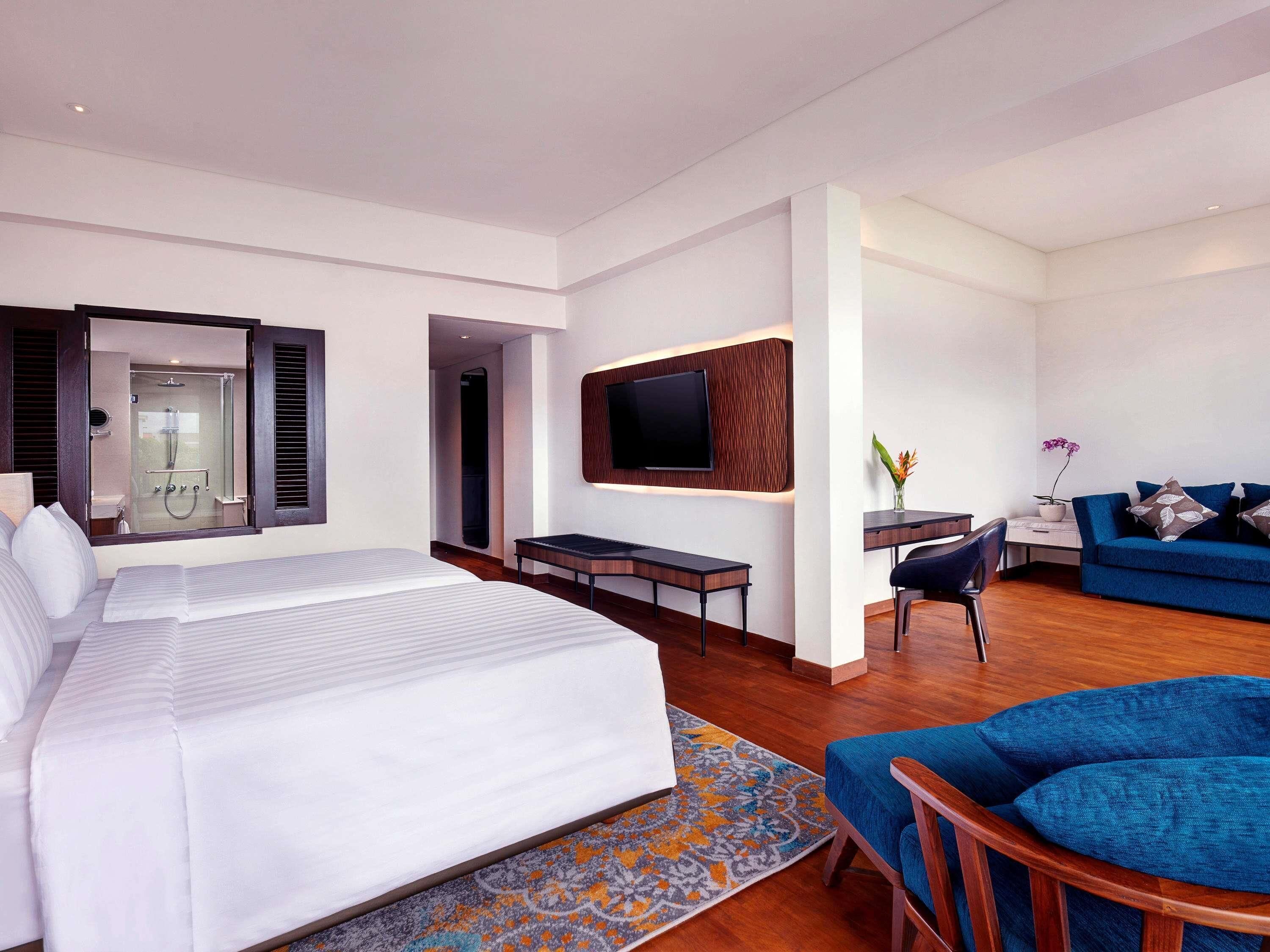 A modern hotel room with a large bed, a desk, a TV, and a sofa.