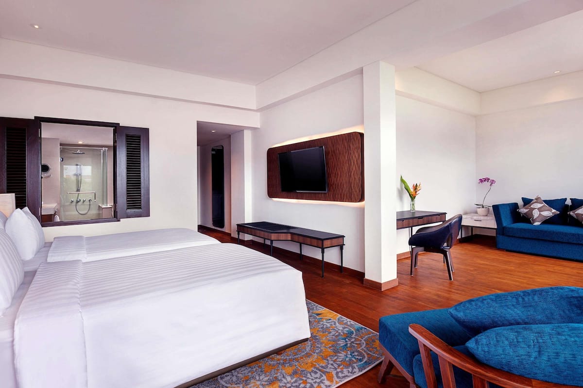 A modern hotel room with a large bed, a desk, a TV, and a sofa.