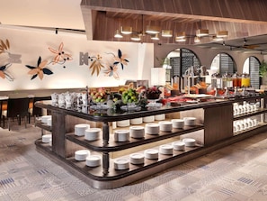 A buffet area with a variety of food items, including fruits and beverages, and a counter with stacked plates. - Grand Mercure Bali Seminyak (Seminyak)