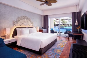 Quarto de hotel moderno com uma cama grande, uma escrivaninha, uma cadeira, uma televisão e vista para uma piscina.