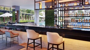 A bar area with a pool view, bar stools, and shelves of bottles. - Grand Mercure Bali Seminyak (Seminyak)
