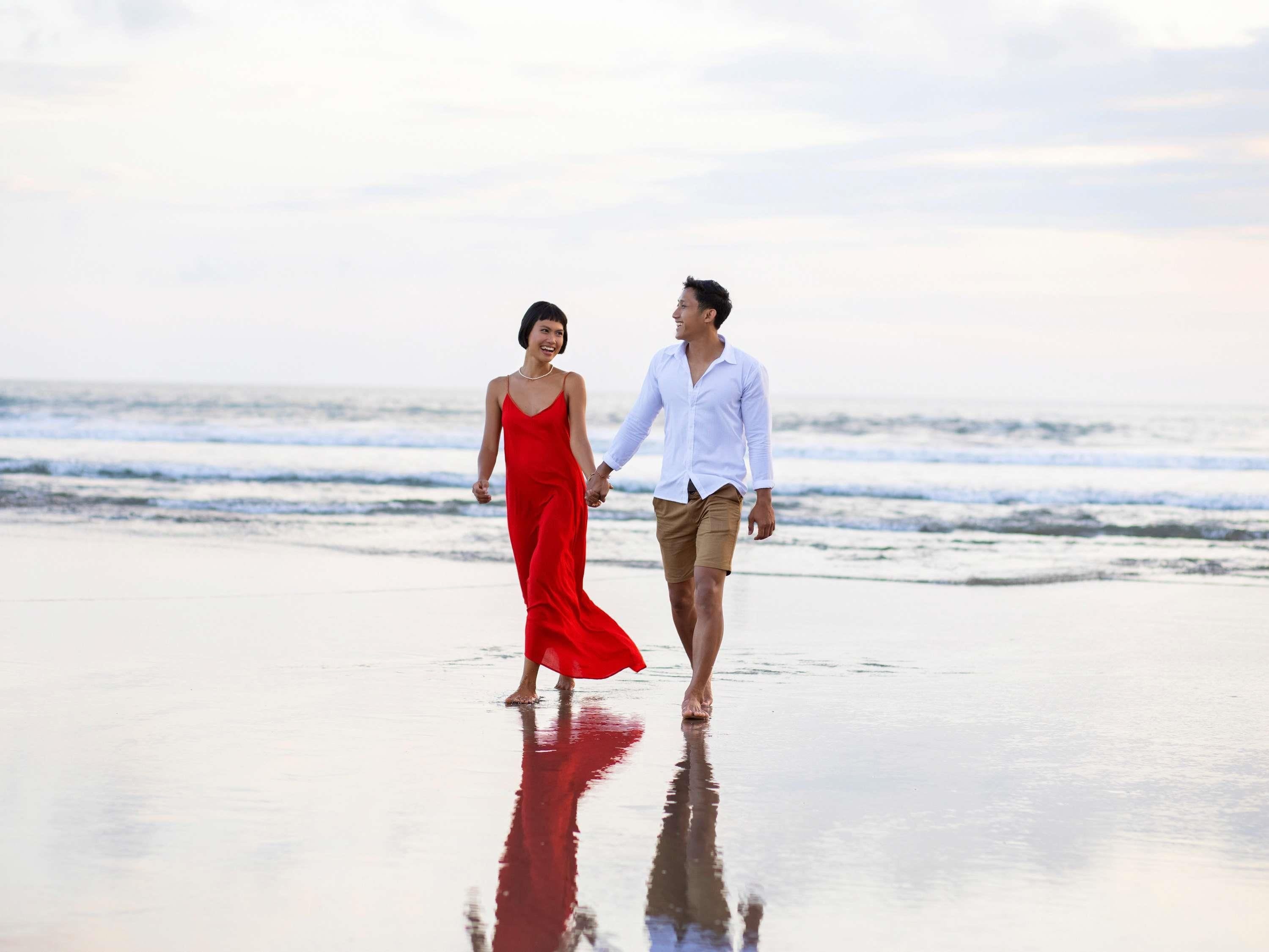 A couple walking on a beach with the ocean in the background.