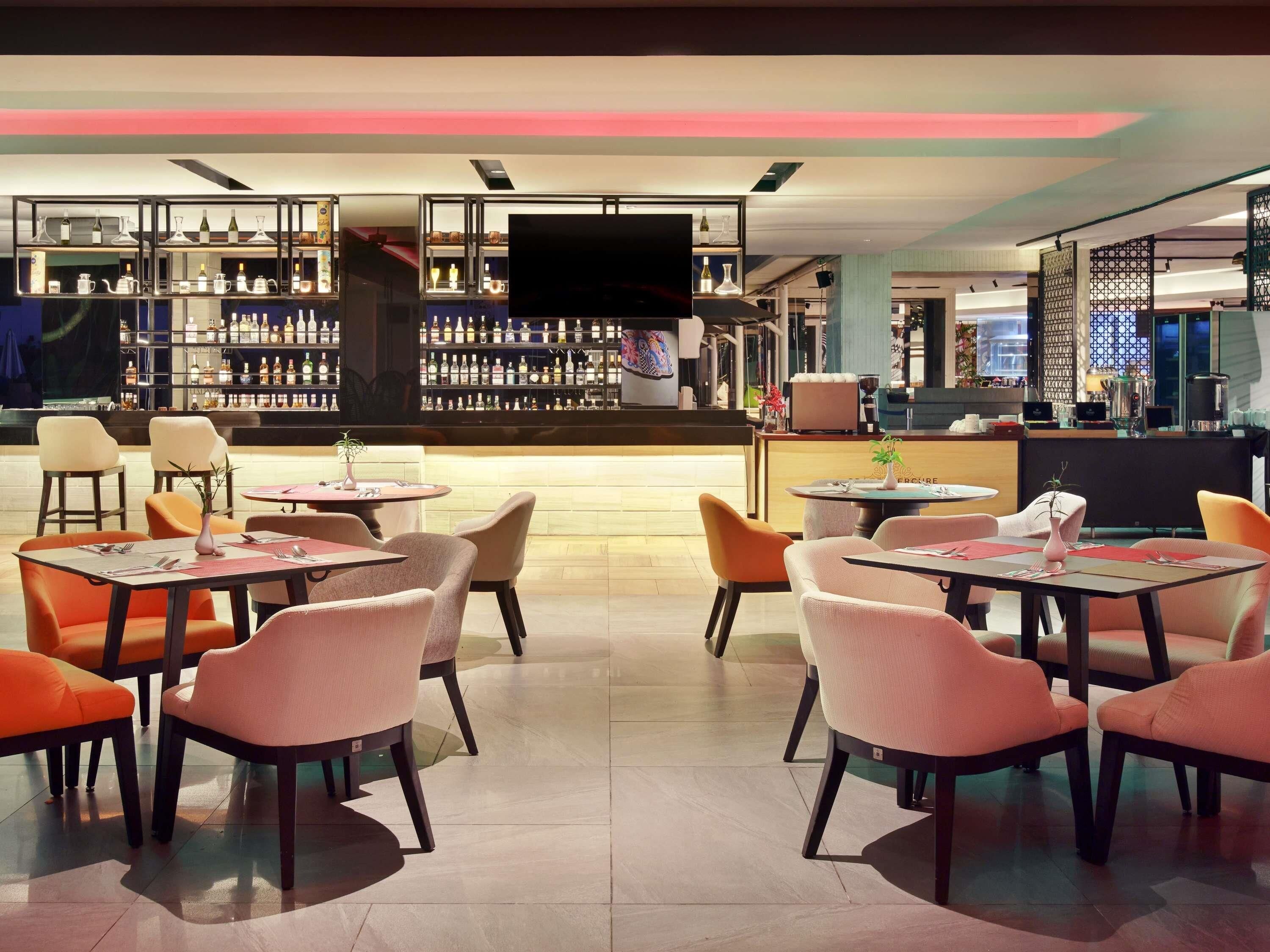 A bar area with multiple tables and chairs, a television screen, and shelves with bottles.