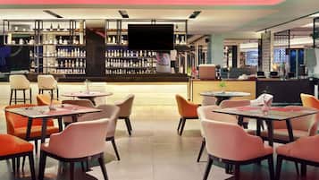 A bar area with multiple tables and chairs, a television screen, and shelves with bottles.