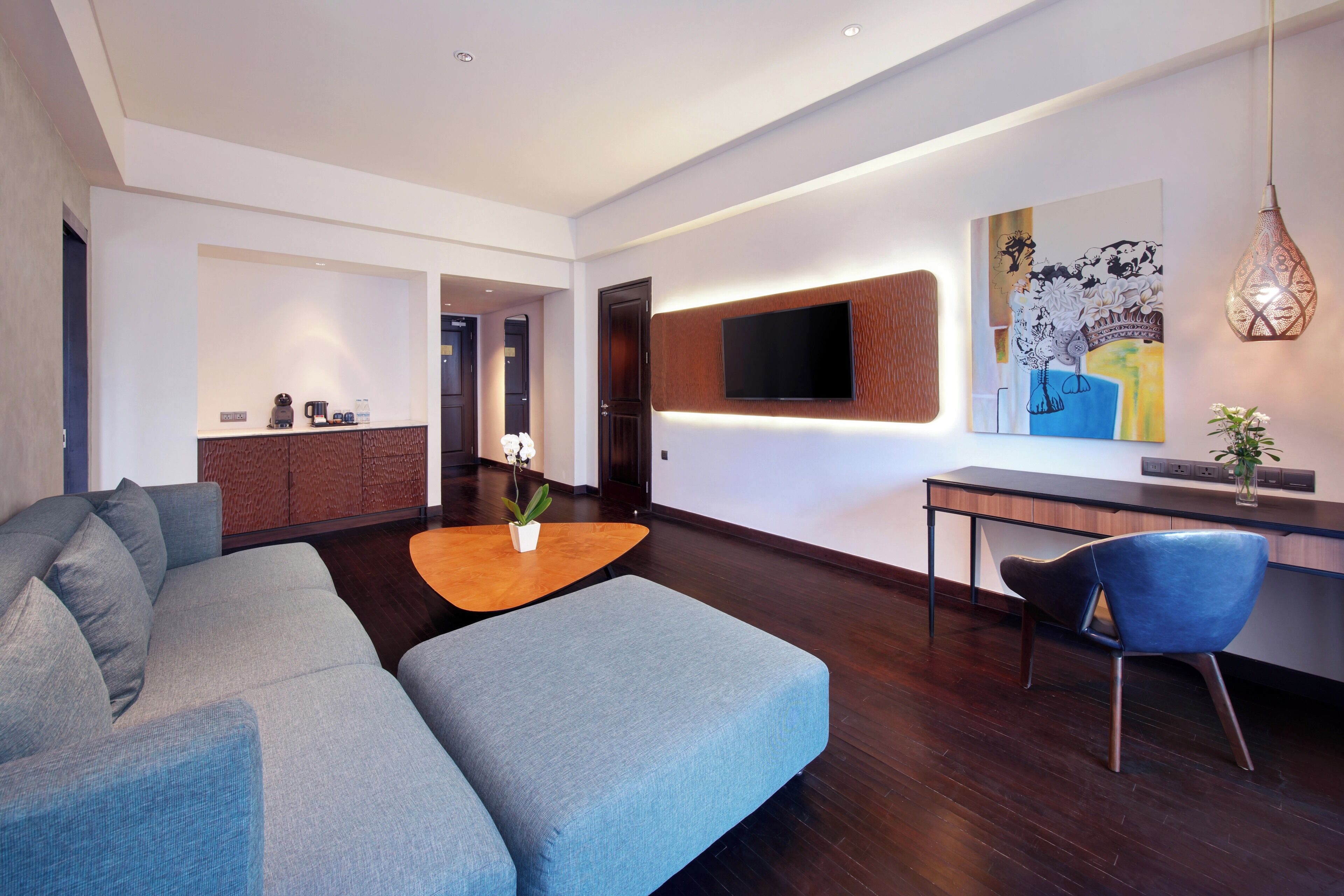Una sala de estar moderna con un sofá seccional, una mesa de centro, un comedor con un televisor montado en la pared y piso de madera.