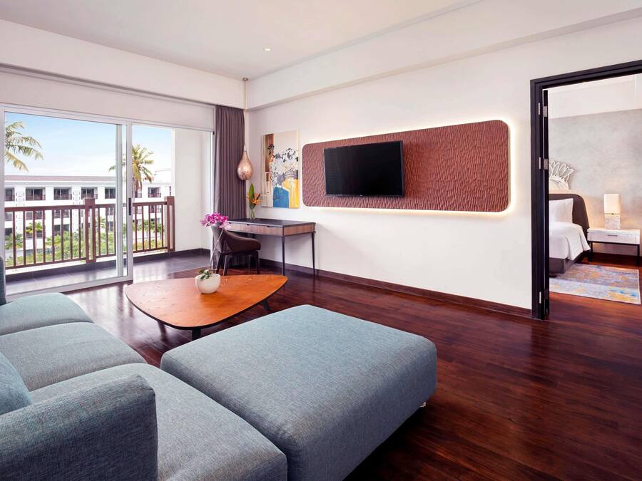 A hotel room with a balcony, a desk, a sofa, a TV, and a bed.