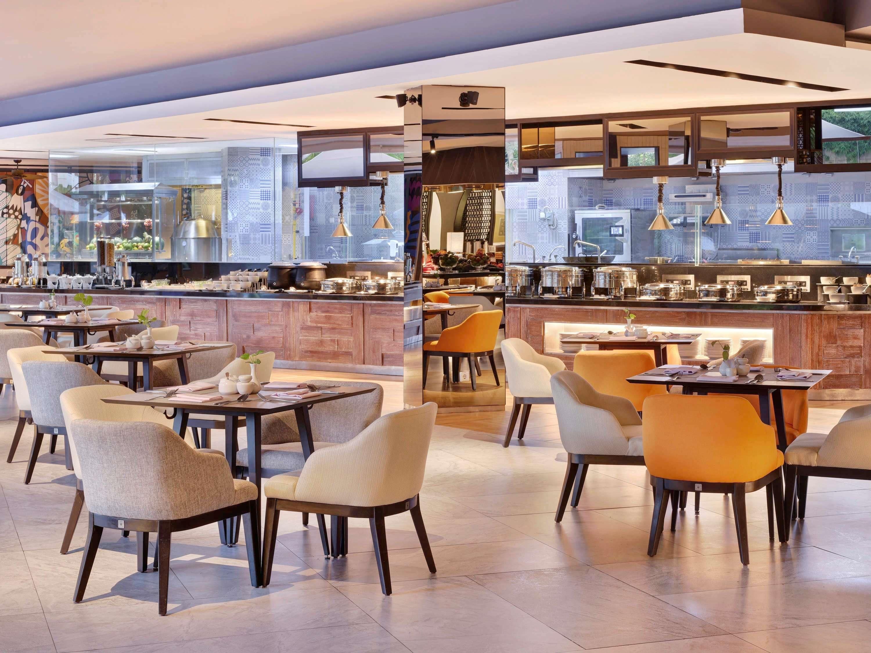 A modern restaurant with a bar area, seating with tables and chairs, and a view of the kitchen through large windows.