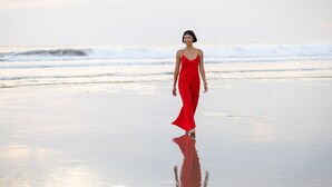 Una persona vestida de rojo caminando por una playa con olas al fondo.