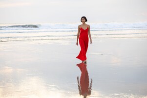 A person in a red outfit walking on a beach with waves in the background.