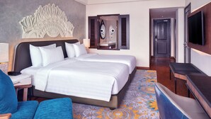 A hotel room with a large bed, a desk with a lamp, a TV, and a decorative wall piece.