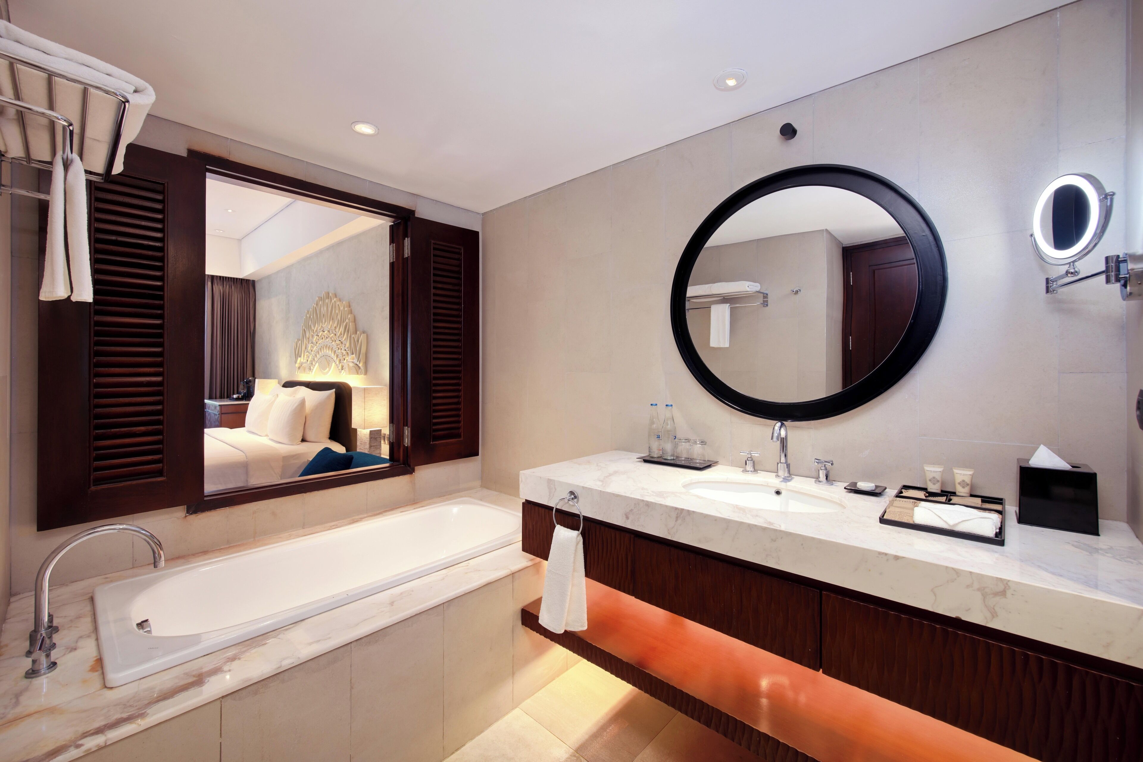 A modern bathroom with a large bathtub, dual sinks, a round mirror, and a towel rack.