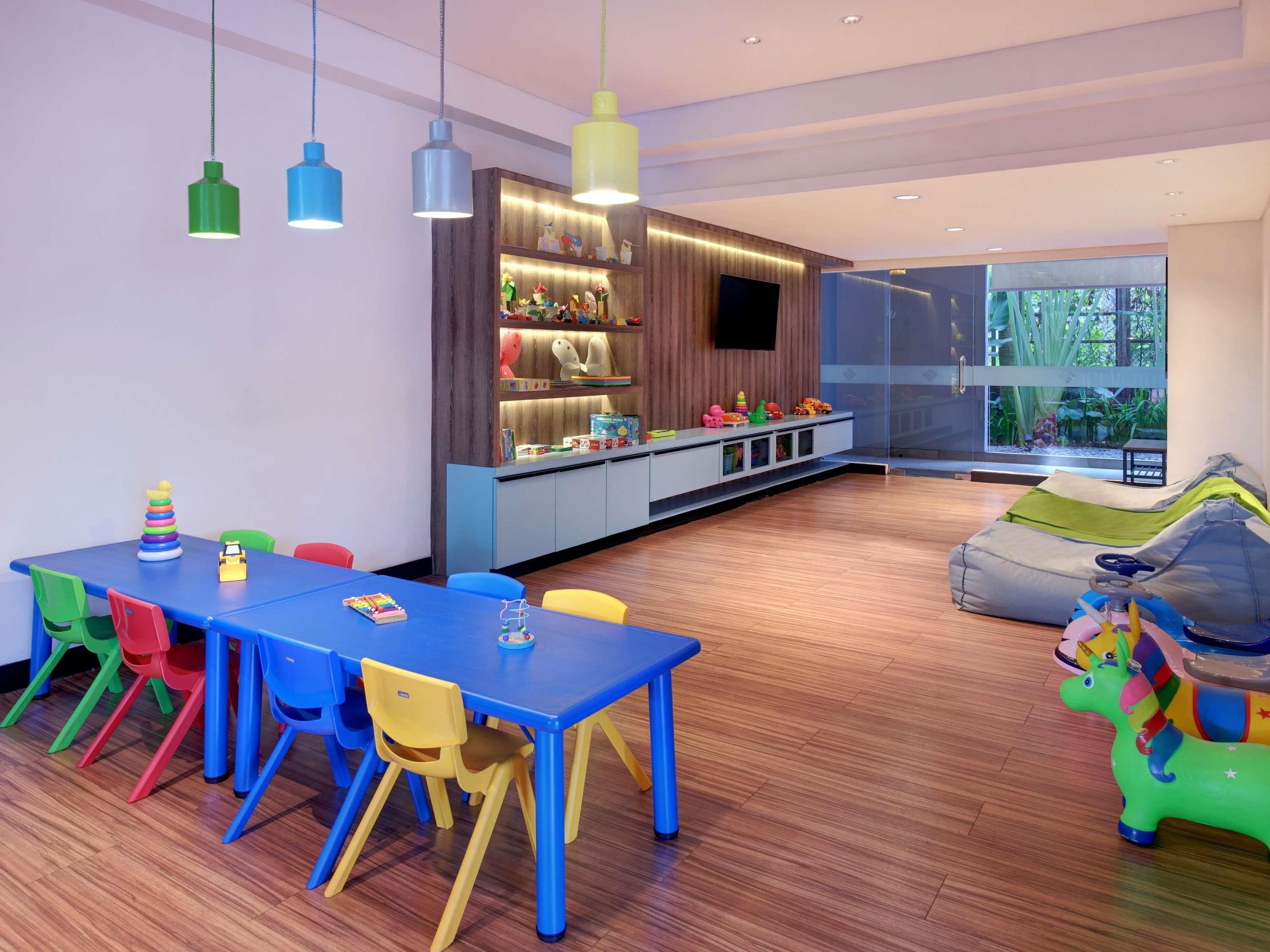 Une salle de jeux moderne pour enfants, avec une table bleue, des chaises colorées et un espace de jeu comprenant un cheval jouet vert.