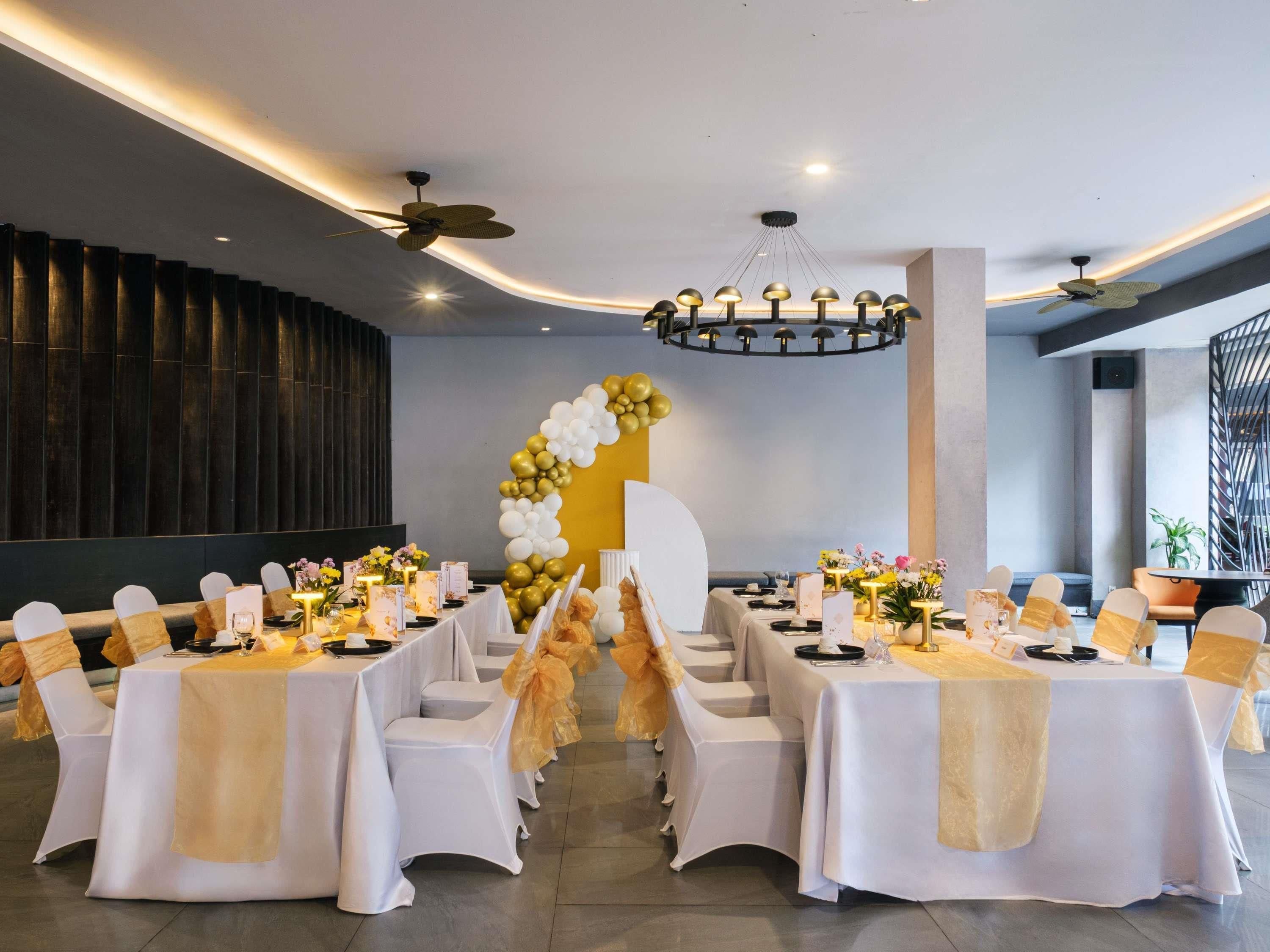 Une salle de banquet avec des tables rondes, des chaises blanches et une arche décorative faite de ballons.