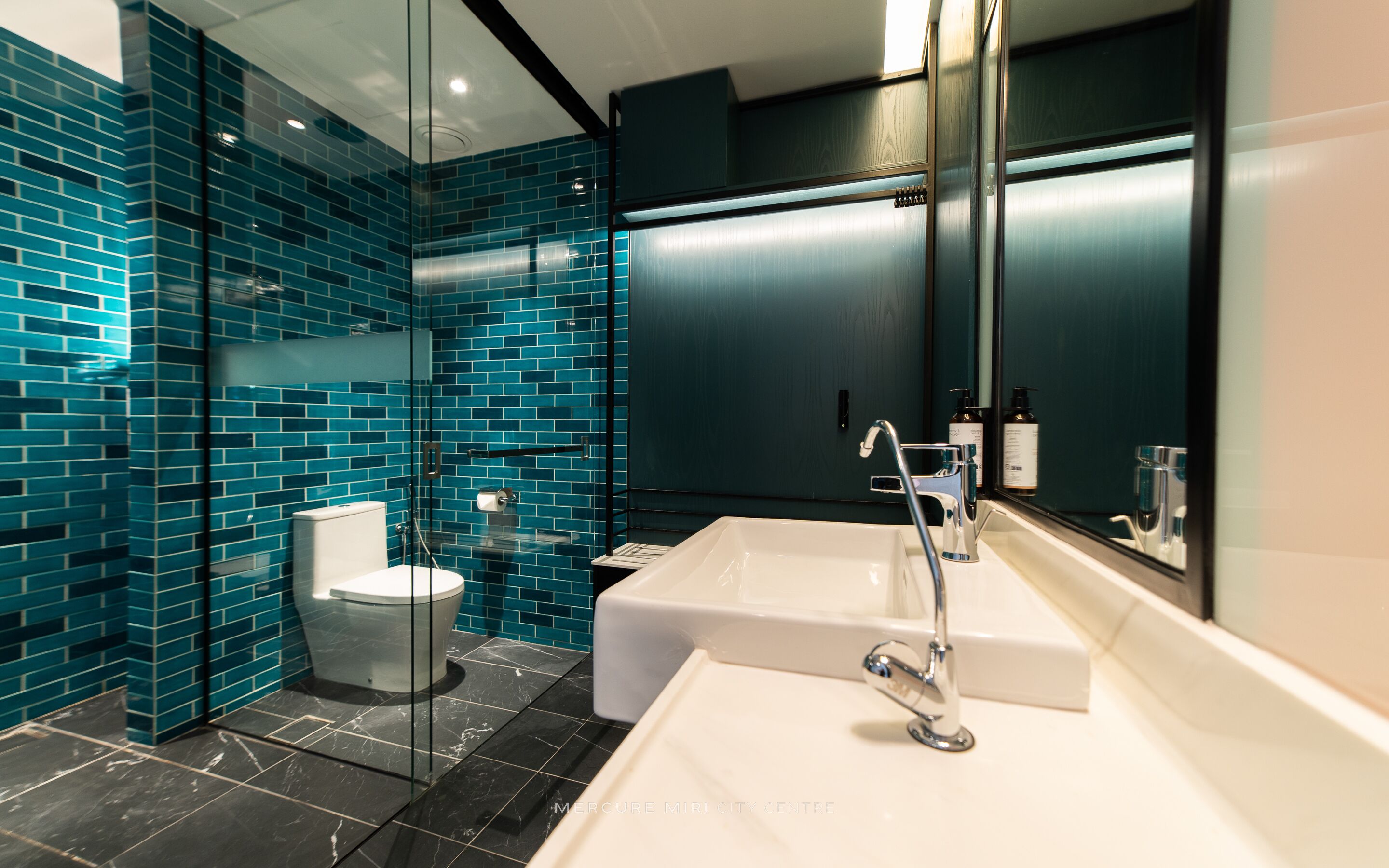 A modern bathroom with a glass shower enclosure, a white sink, and a dark tiled wall.