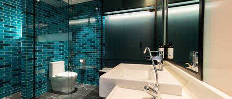A modern bathroom with a glass shower enclosure, a white sink, and a dark tiled wall.