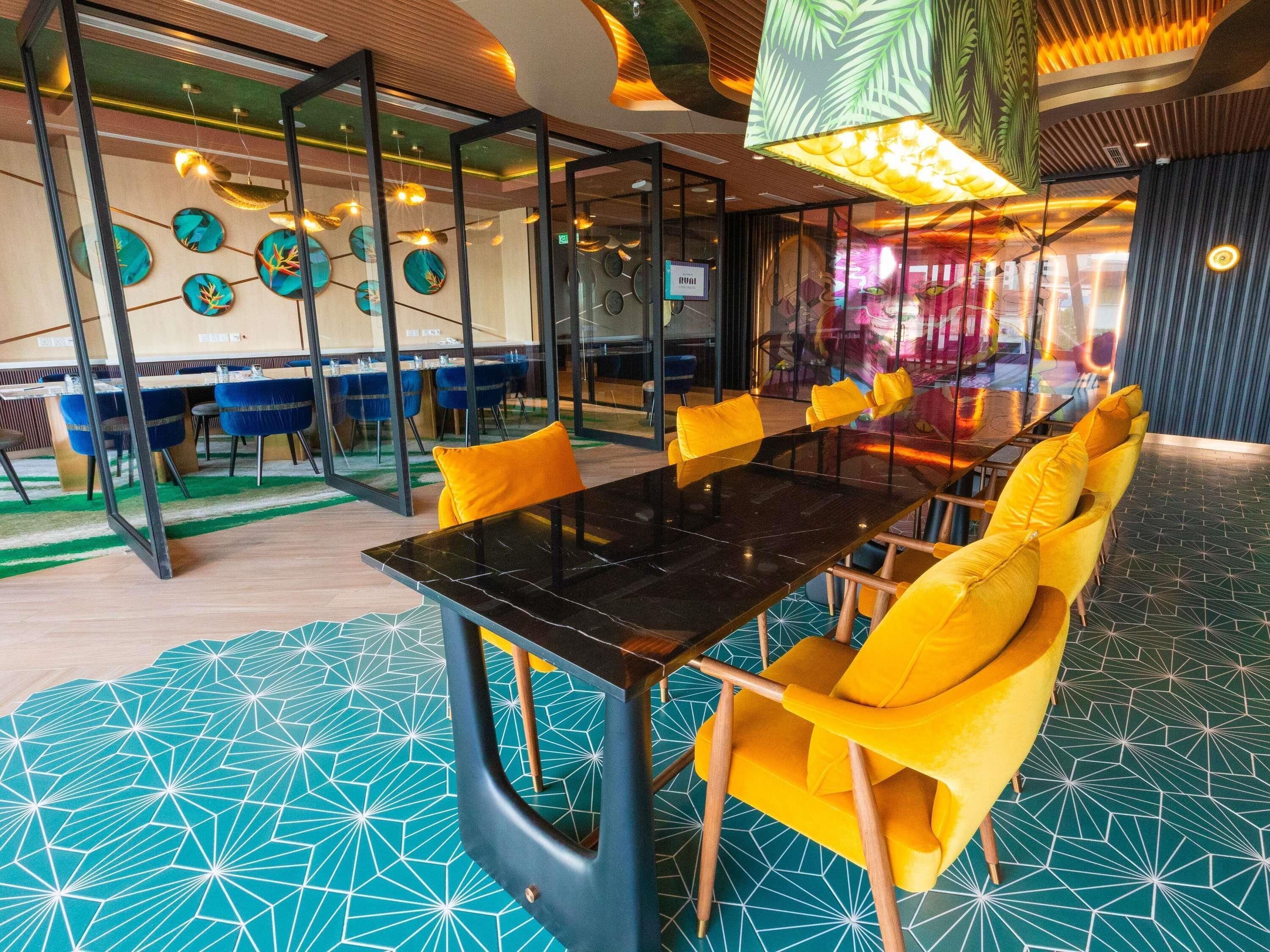 A modern dining area with a long table, yellow chairs, and a patterned floor.