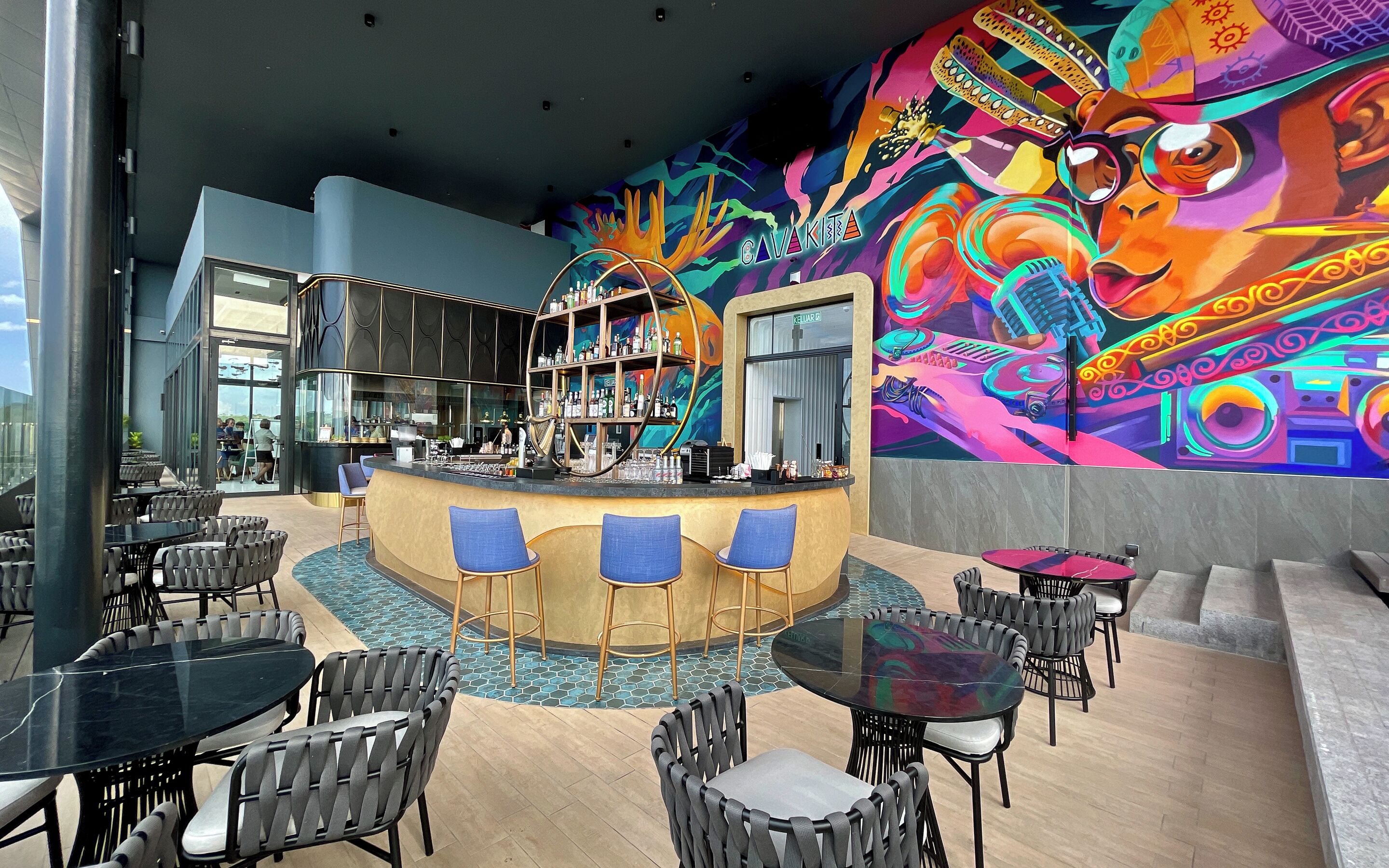 A modern bar area with a colorful mural, bar stools, and a seating area with tables and chairs.