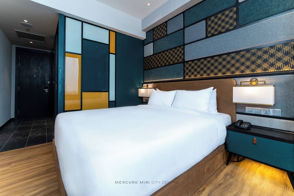 A hotel room with a large bed, a nightstand with a lamp, and a patterned wall design.