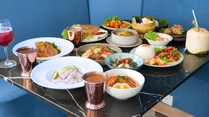 A table set with various dishes, drinks, and a coconut drink on a blue sofa.