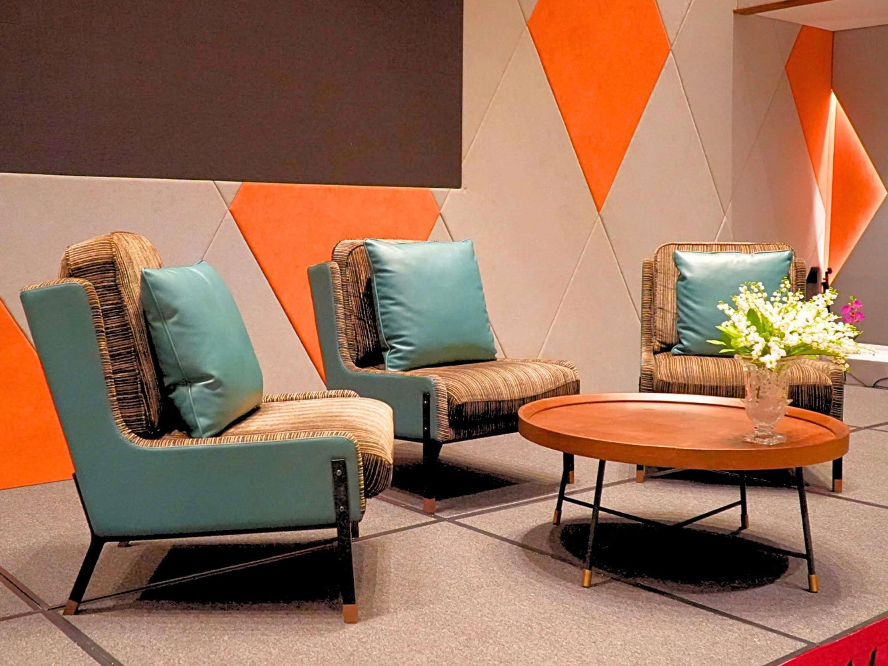 A modern lounge area with two armchairs and a round coffee table, featuring a geometric wall design and a vase with flowers.