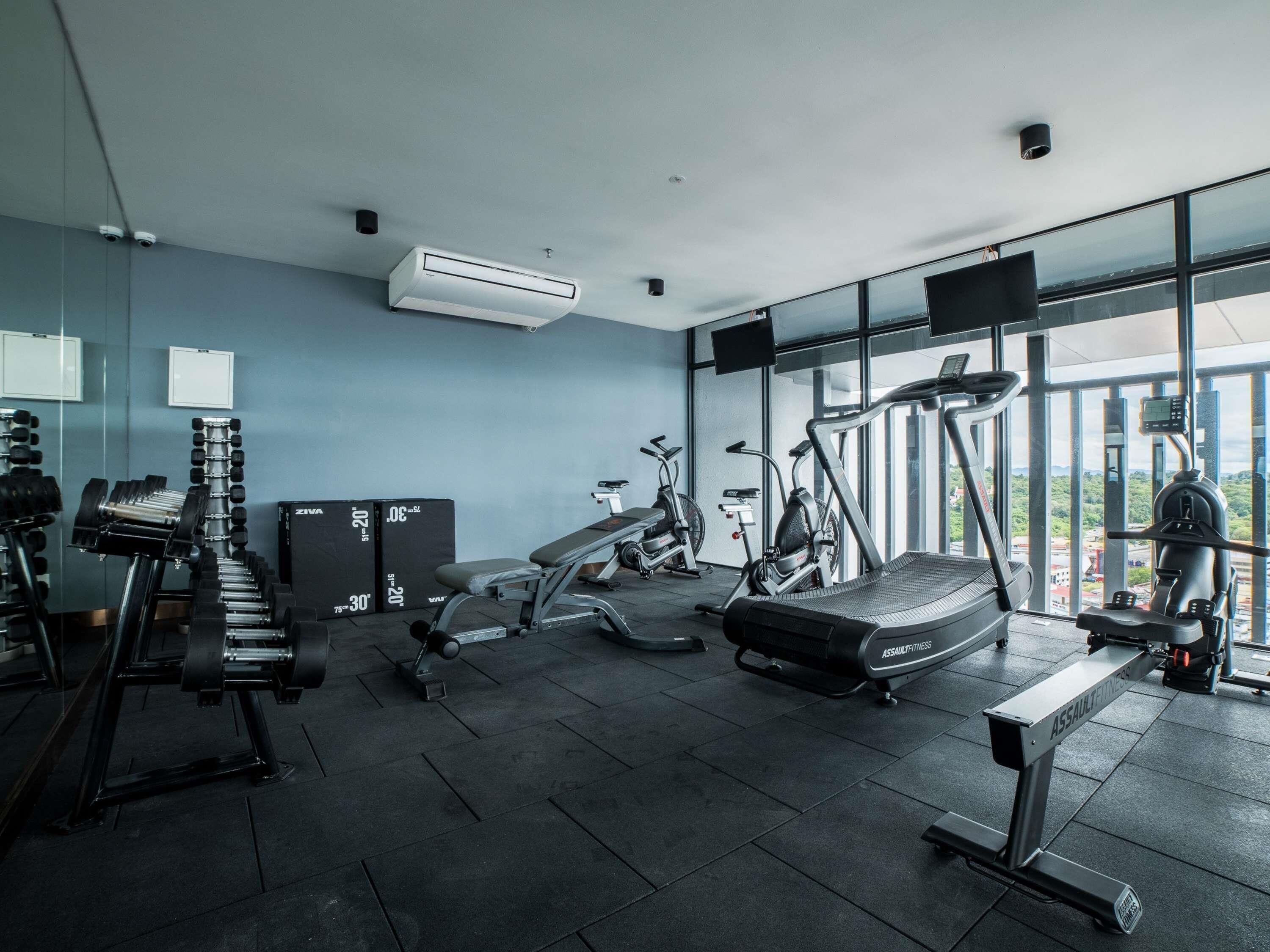 A modern gym with exercise equipment, large windows, and an air conditioning unit.