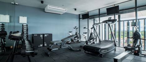 A modern gym with exercise equipment, large windows, and an air conditioning unit.