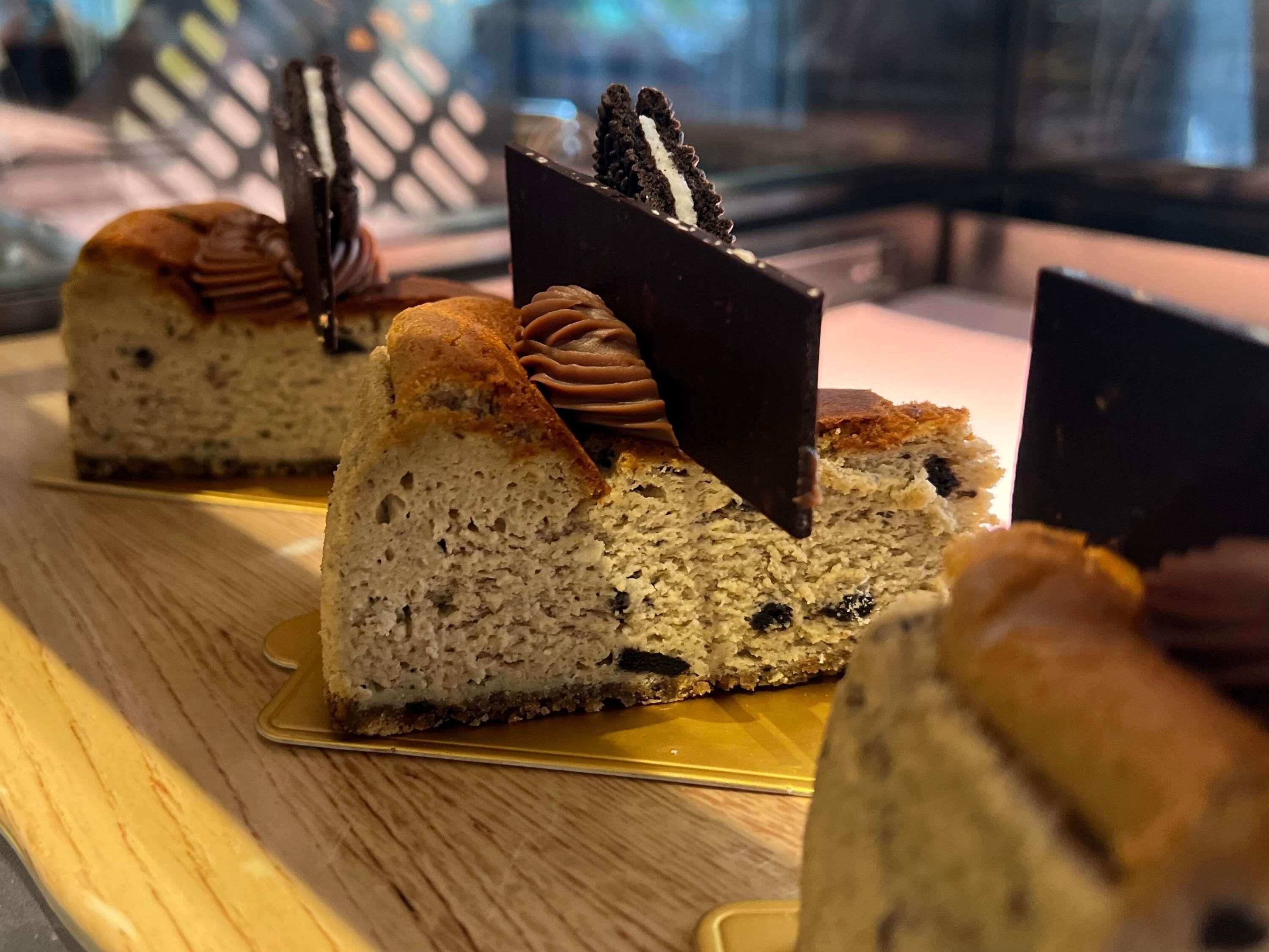 Una porción de pastel de queso con cobertura de chocolate y galletas, sobre un plato dorado.