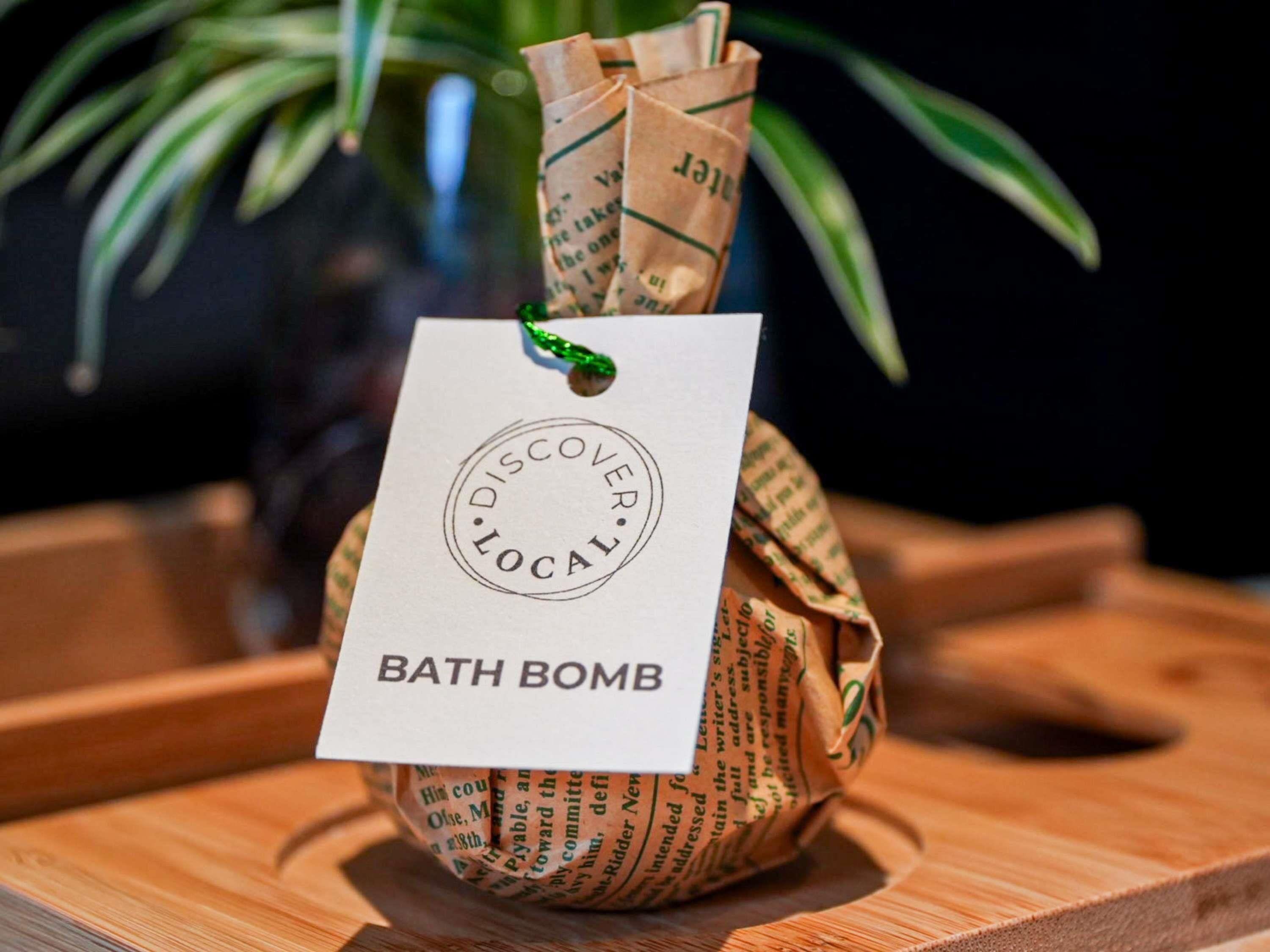 A wooden bowl with a tag labeled 'BATH BOMB' and a green ribbon.