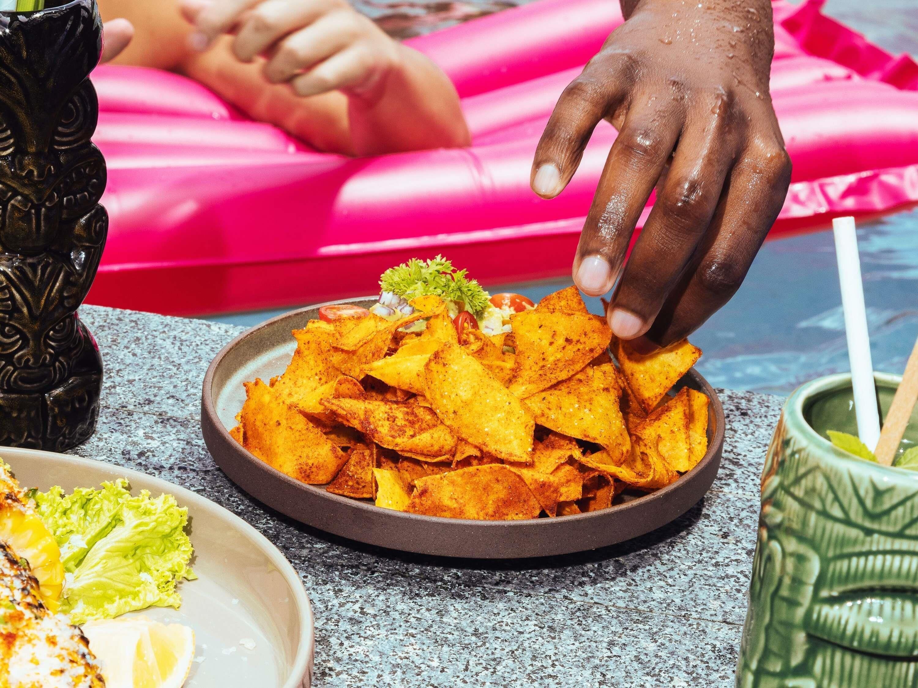 A plate of seasoned tortilla chips with a garnish, a bowl of grilled chicken, and a green drink in a ceramic cup.