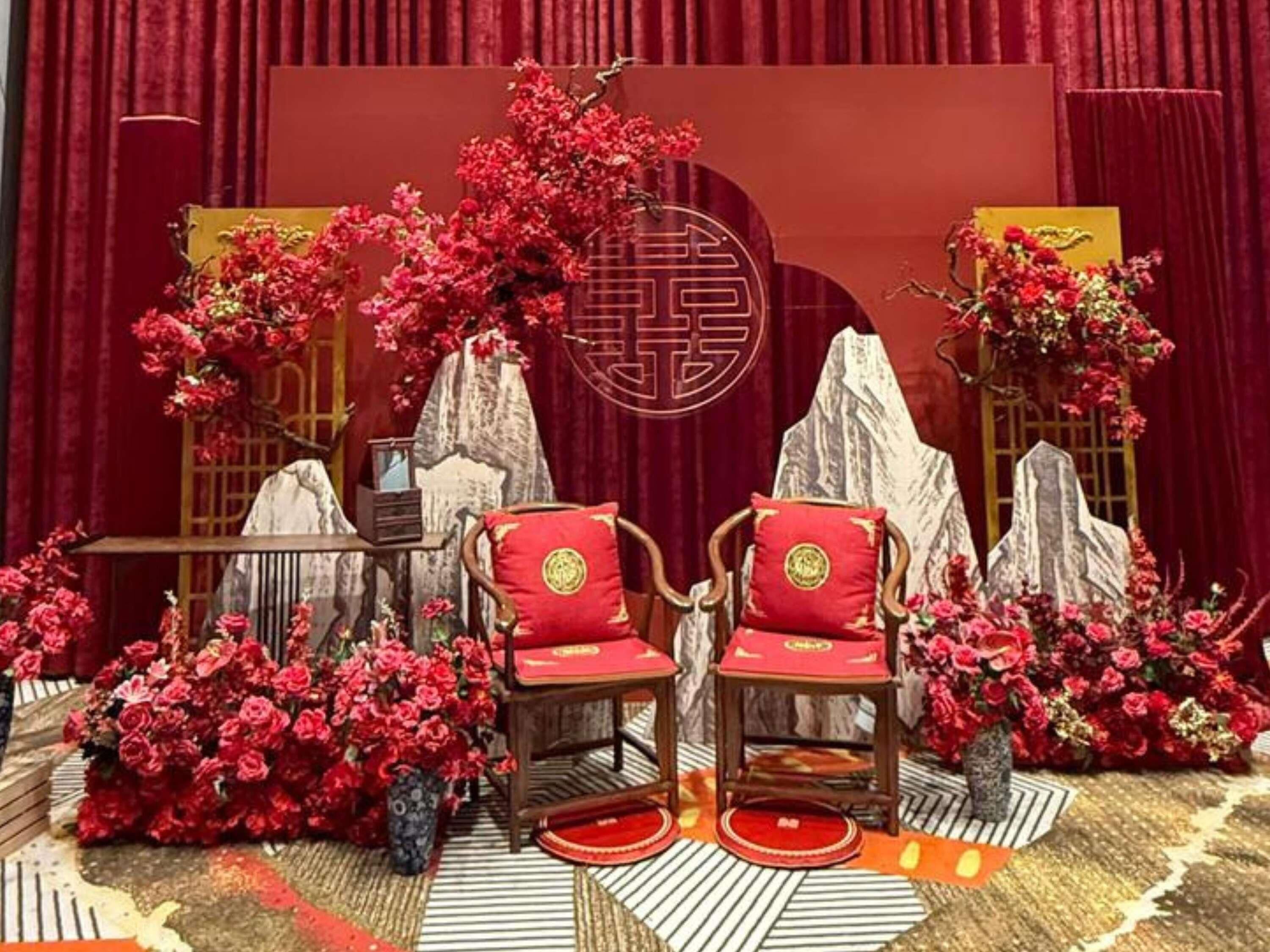 Una habitación decorada con un estilo tradicional, que incluye sillas rojas, un telón rojo de fondo y arreglos florales.