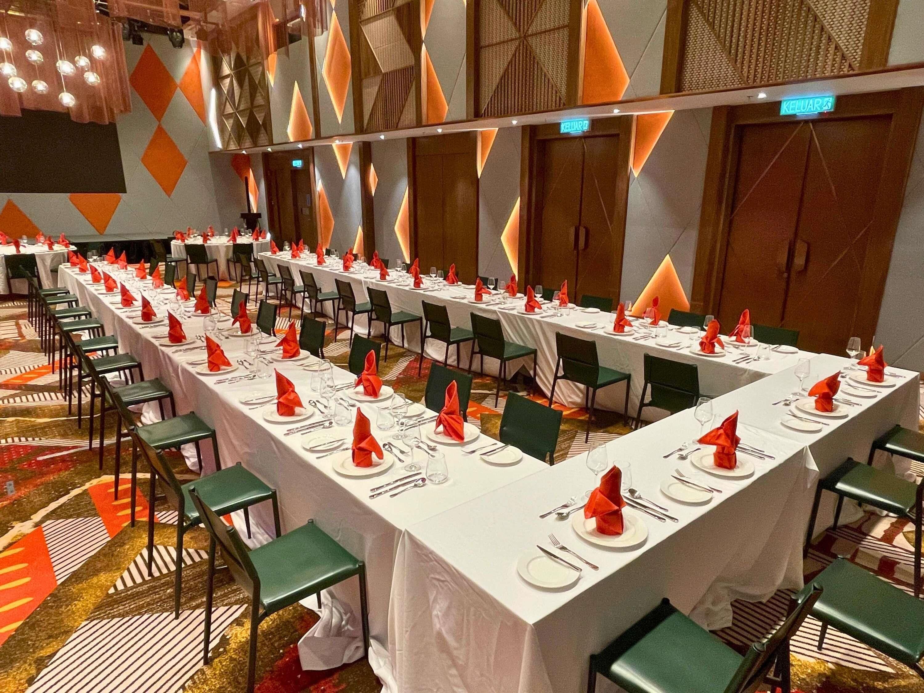 A conference room with long tables set for a formal event, equipped with chairs, tables, and a carpeted floor.