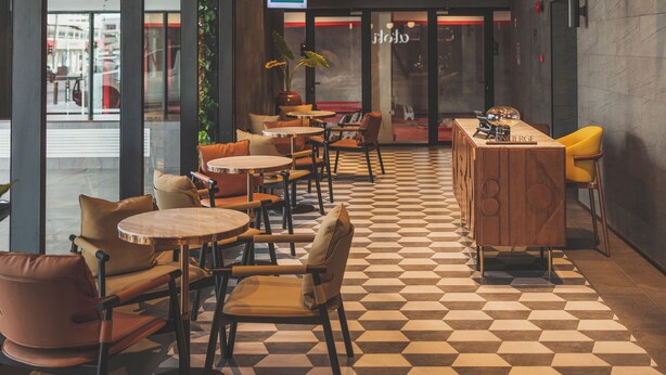A spacious indoor area with a checkered floor, wooden furniture, and a large screen displaying information.