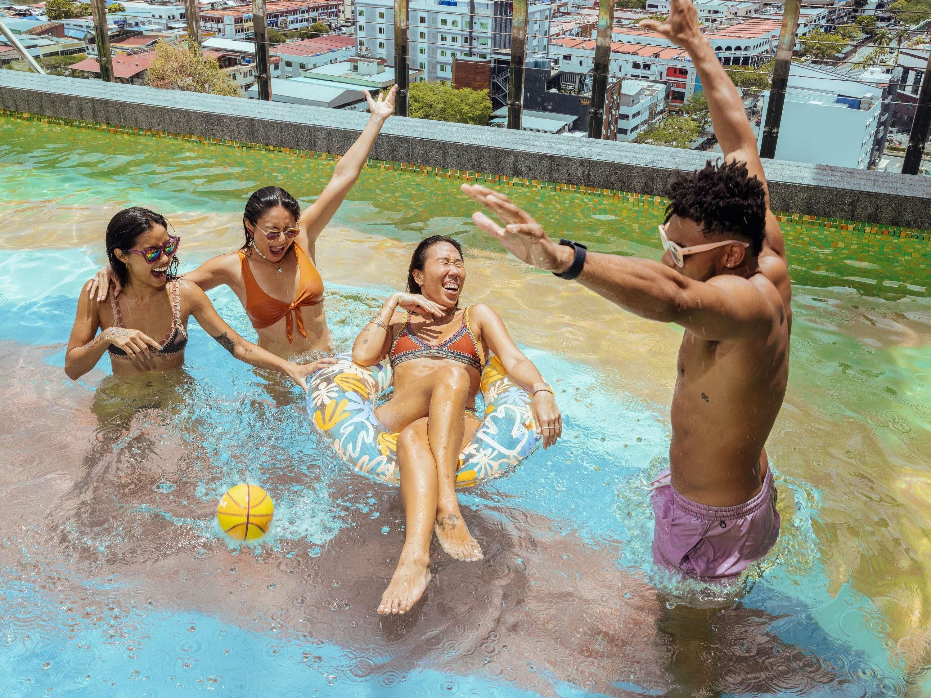 Une piscine où des gens s’amusent, entourée d’immeubles.