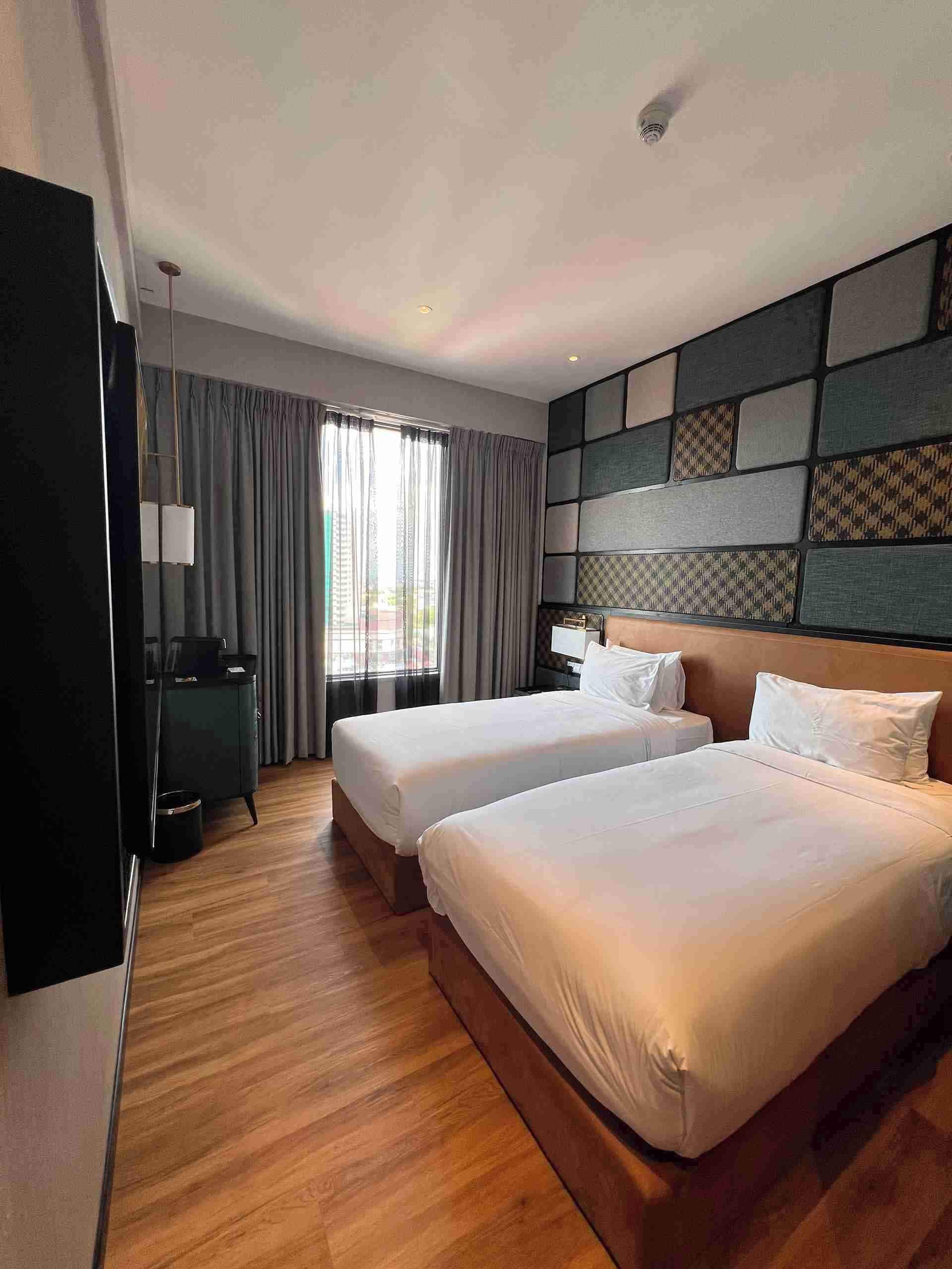 A hotel room with two beds, a desk, a chair, a wardrobe, and a large window with curtains.