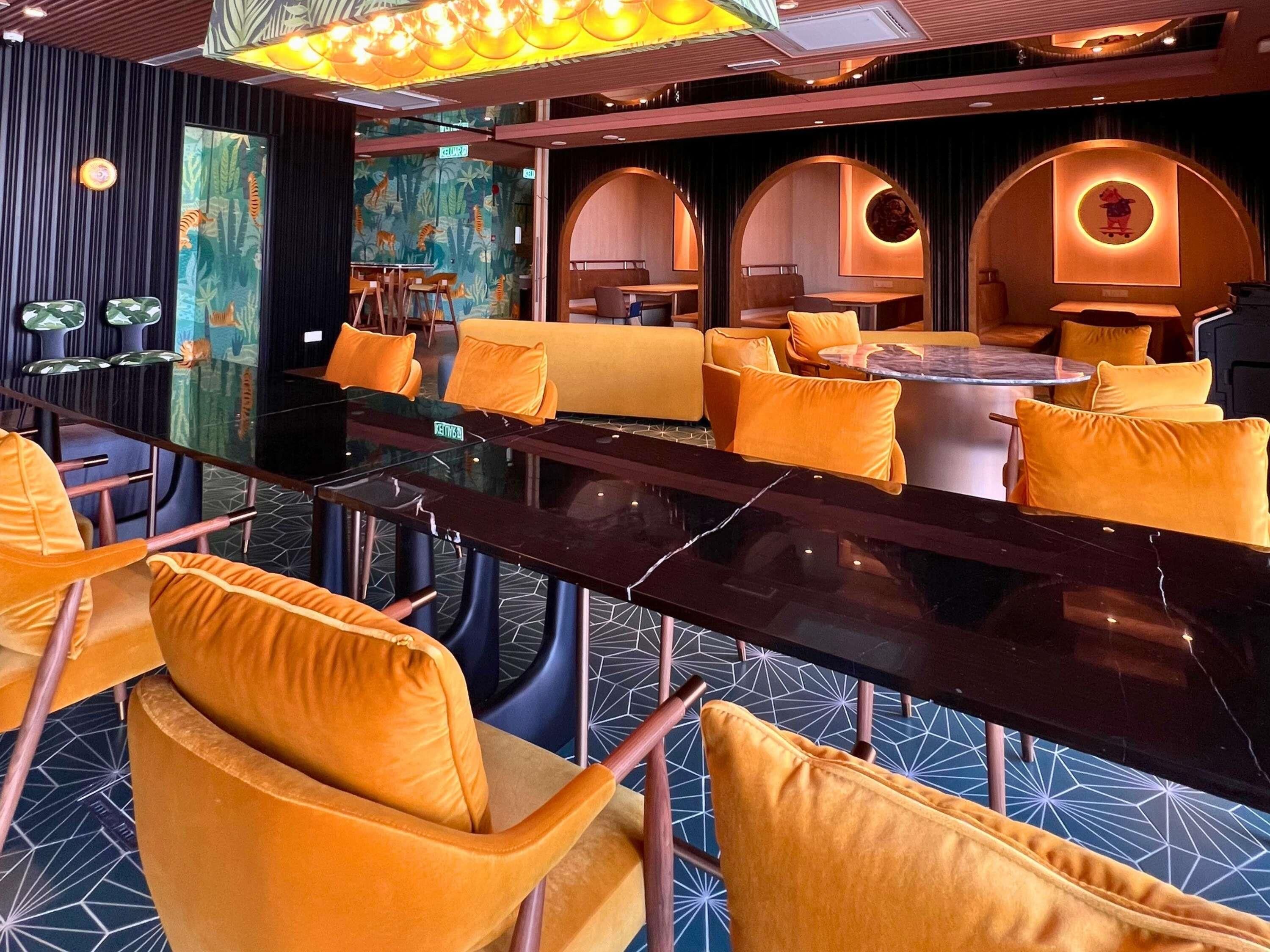 A modern lounge area with a long table, yellow chairs, and a mural wall.
