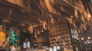 A modern bar area with a high ceiling, wooden paneling, and a mural on the wall.