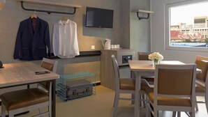 Habitación de hotel moderna con zona de comedor, televisor montado en la pared y ventana con vista a la ciudad.