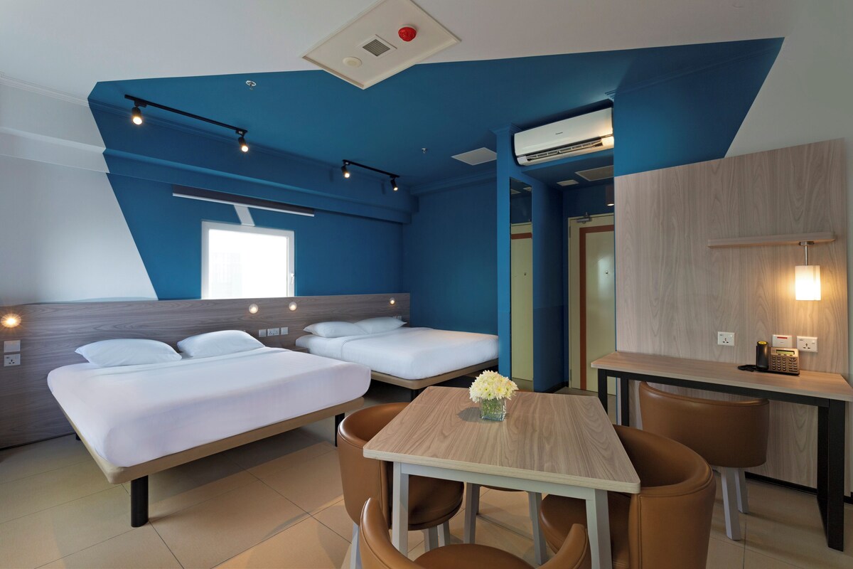 Une chambre d’hôtel moderne avec un lit en mezzanine, une table à manger et une petite kitchenette.