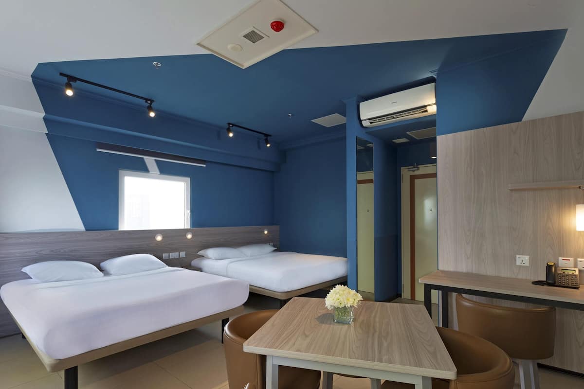 A modern hotel room with a bed, a small dining table, and a seating area.
