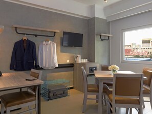 Habitación de hotel moderna con zona de comedor, televisor montado en la pared y ventana con vista a la ciudad.